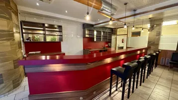 Eine moderne Bar mit roter Theke, Holzverkleidung und Barhockern, beleuchtet von Hängelampen.