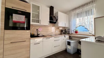 Moderne Küche mit weißen Hochglanzfronten, Holzakzenten und Fenster für natürliches Licht.