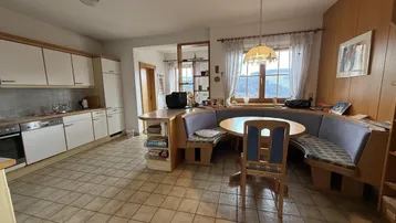 Geräumige Wohnküche mit integriertem Essbereich, Fliesenboden und Blick ins Grüne durch das Fenster.