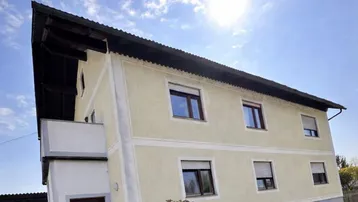 Gelb gestrichenes Einfamilienhaus mit Satteldach und kleinem Balkon unter blauem Himmel.