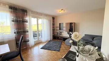 Helles Wohnzimmer mit Parkettboden, Zugang zum Balkon und weitem Blick ins Grüne.