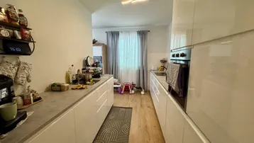 Moderne Küche mit weißen Hochglanzfronten, integrierten Geräten und hellem Laminatboden.