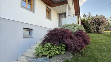 Seitenansicht des Hauses mit Steintreppe, üppiger Bepflanzung und kleinem Balkon.