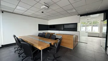 Moderner Konferenzraum mit großem Holztisch, Projektor und mehreren Bildschirmen für Präsentationen.