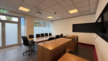 Geräumiger Konferenzraum mit großem Holztisch, bequemen Stühlen und integriertem Beamer für Präsentationen.