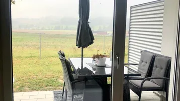 Möblierte Terrasse mit Esstisch und Blick auf die grüne Landschaft.