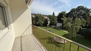 Balkon mit Blick auf den grünen Gemeinschaftsgarten und Kinderspielplatz.