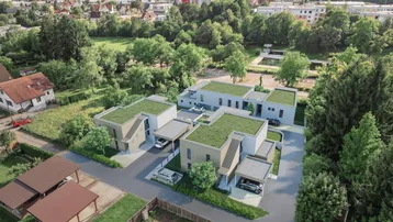 Moderne Häuser mit begrünten Flachdächern und Carports in einer grünen Wohnsiedlung.
