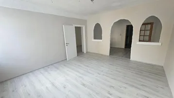 Helles, unmöbliertes Zimmer mit Laminatboden und dekorativen Rundbögen, frisch renoviert.