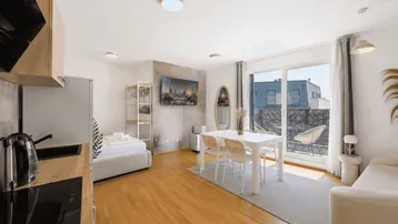Helles, offenes Studio-Apartment mit integrierter Küche, Essbereich und Zugang zu einem Balkon.