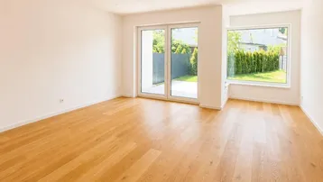 Heller, leerer Raum mit Holzboden, großen Fenstern und Zugang zu einer kleinen Terrasse.