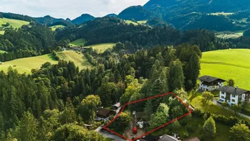 Luftaufnahme eines Grundstücks mit roter Umrandung, umgeben von Wäldern und Bergen.