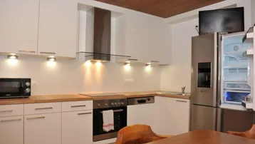 Moderne Küche mit weißen Schränken, Holzarbeitsplatte und integrierten Edelstahlgeräten.