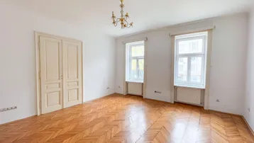 Helles Zimmer mit Fischgrätparkett, hohen Fenstern und einem klassischen Kronleuchter.
