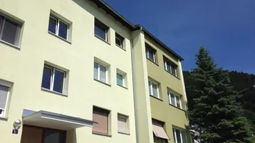 Mehrstöckiges Wohngebäude mit hellgrüner Fassade unter blauem Himmel.