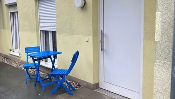 Eingangsbereich des Gebäudes mit einer kleinen blauen Sitzgruppe und Rollläden an den Fenstern.