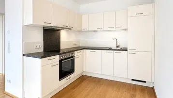 Moderne Einbauküche mit hellen Schränken, dunkler Arbeitsplatte und Holzfußboden in einem offenen Wohnbereich.