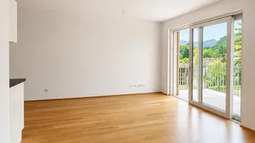 Lichtdurchfluteter Wohnbereich mit großen Schiebetüren, die auf einen Balkon mit grüner Aussicht führen.