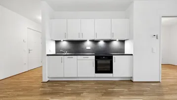 Moderne Einbauküche mit weißen Schränken, dunkler Arbeitsplatte und integriertem Backofen.