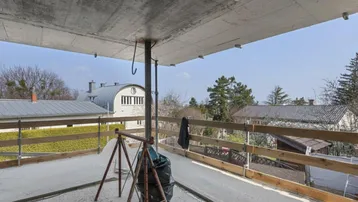 Baustelle mit Rohbau einer Terrasse und Blick auf umliegende Häuser und Bäume.