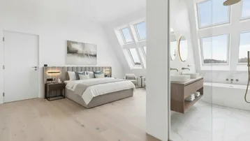 Helles Schlafzimmer mit Holzboden, großen Dachfenstern und offenem Badbereich mit Doppelwaschbecken und Badewanne.