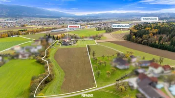 Luftaufnahme des Anwesens mit umrandetem Grundstück, umgeben von Wiesen, Wald und Bergen in der Ferne.