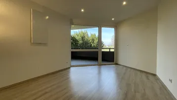 Helles Wohnzimmer mit modernem Laminatboden, Einbaustrahlern und Zugang zu einem Balkon mit grüner Aussicht.