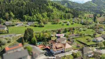 Luftaufnahme der Immobilie in ländlicher Umgebung mit viel Grün und Bergen im Hintergrund.