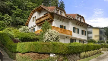 Traditionelles Haus mit gepflegtem Garten und Holzbalkonen an einem grünen Hang gelegen.