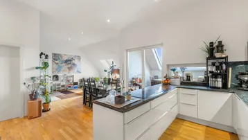 Helle offene Küche mit Essbereich, Holzboden und Zugang zu einem Balkon oder einer Terrasse.