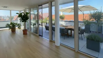 Helles Wohnzimmer mit Holzboden und großen Fensterfronten, die Zugang zu einer möblierten Dachterrasse bieten.