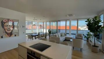 Offener Wohn-Essbereich mit moderner Kücheninsel, Holzboden und weitem Blick über die Stadt.