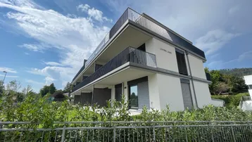 Modernes Mehrfamilienhaus mit Balkonen und Blick auf die Umgebung unter blauem Himmel.