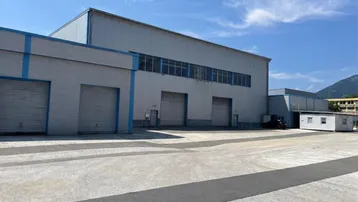 Großes Industriegebäude mit mehreren Rolltoren und weitem Vorplatz unter blauem Himmel.