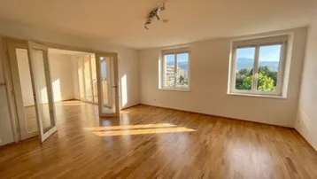 Helles Wohnzimmer mit Parkettboden, großen Fenstern und Blick auf die umliegende Landschaft.