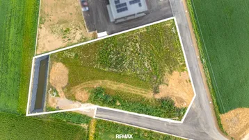 Luftaufnahme eines unbebauten Grundstücks mit weißer Umrandung, umgeben von grünen Feldern und einer Straße.
