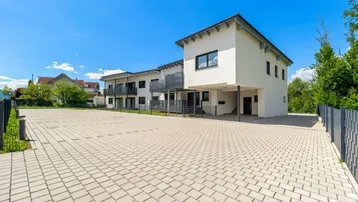 Modernes Mehrfamilienhaus mit gepflastertem Parkplatz und klarer Architektur unter blauem Himmel.