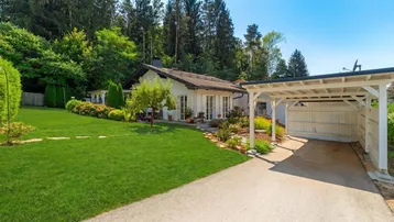 Haus mit großem Garten, gepflegtem Rasen und einem Carport unter blauem Himmel.