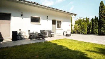 Helle Hausfassade mit gepflegtem Rasen und möblierter Terrasse für entspannte Stunden im Freien.