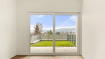 Heller Raum mit Holzboden, großen Schiebetüren und Zugang zu einer Terrasse mit Garten und Bergblick.
