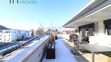 Große, sonnige Terrasse mit Sitzgelegenheiten und Bergblick, teilweise mit Schnee bedeckt.