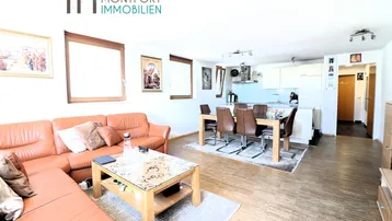 Heller offener Wohn-Essbereich mit Ledersofa, Esstisch und integrierter Küche.