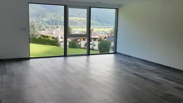 Geräumiger Wohnbereich mit großen Fenstern, die einen weiten Blick auf die grüne Landschaft und die Berge bieten.