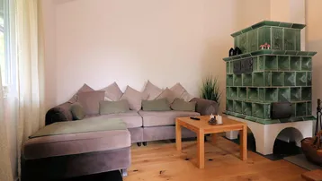 Wohnzimmer mit bequemem Sofa, Holztisch und einem traditionellen grünen Kachelofen als Blickfang.