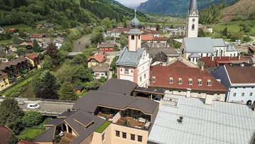 Luftaufnahme einer malerischen Stadt mit Bergen, Fluss und einem Gebäude mit moderner Dachterrasse.