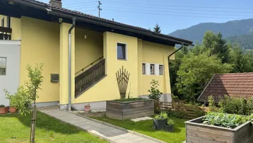 Gelbe Hausfassade mit Außentreppe und gepflegtem Vorgarten in ländlicher Umgebung.