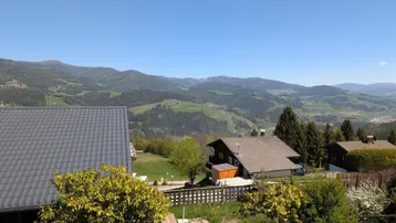 Weitläufiger Panoramablick auf die umliegende Berglandschaft und grüne Täler unter blauem Himmel.