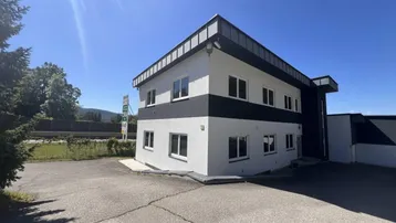Modernes Geschäftsgebäude mit weißer und schwarzer Fassade unter strahlend blauem Himmel.