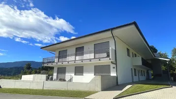 Modernes Mehrfamilienhaus mit weißer Fassade, Balkonen und Blick auf die umliegende Landschaft.