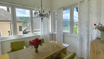 Heller Essbereich mit großzügigen Fenstern, Kronleuchter und Blick auf den See und die Berge.